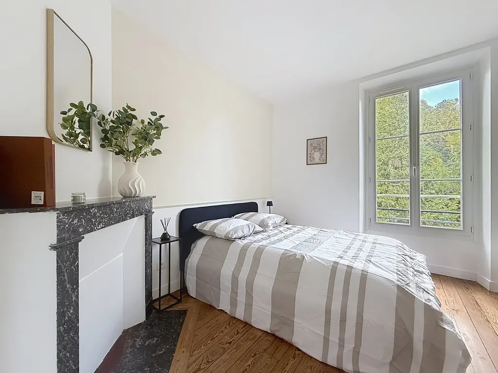 Chambre avec cheminée en marbre noir, parquet et fenêtre sur la verdure