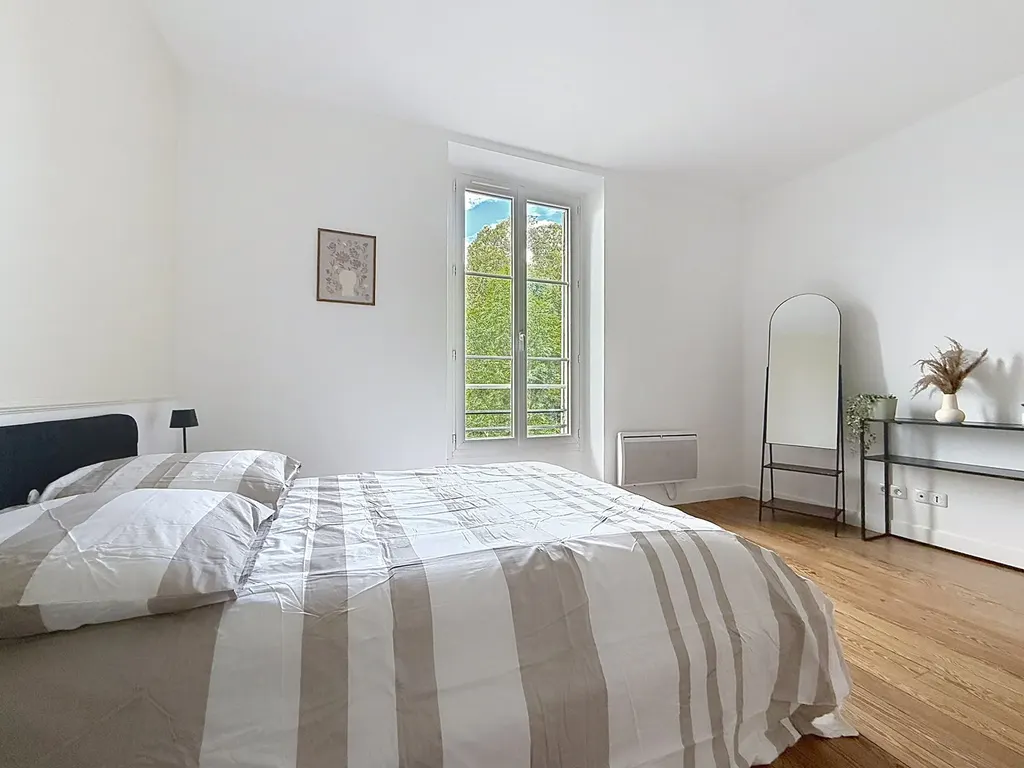 Chambre avec lit, miroir en arche et fenêtre ouverte sur les arbres