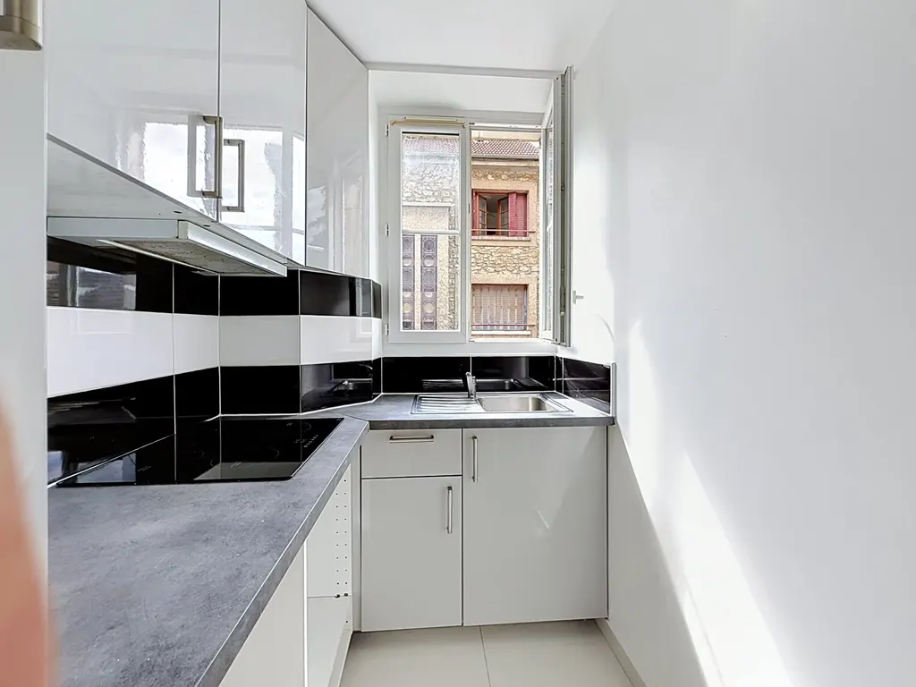 Cuisine en longueur avec meubles blancs, plaque à induction et fenêtre