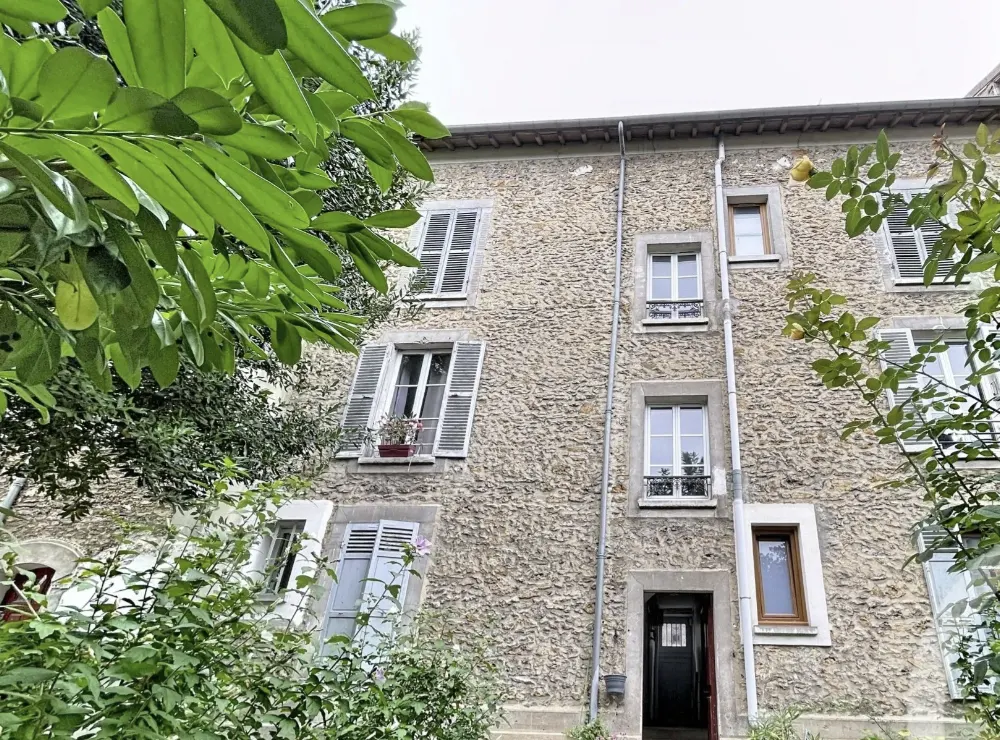 Façade arrière de l'immeuble en meulière vue du jardin, volets gris et porte d'entrée