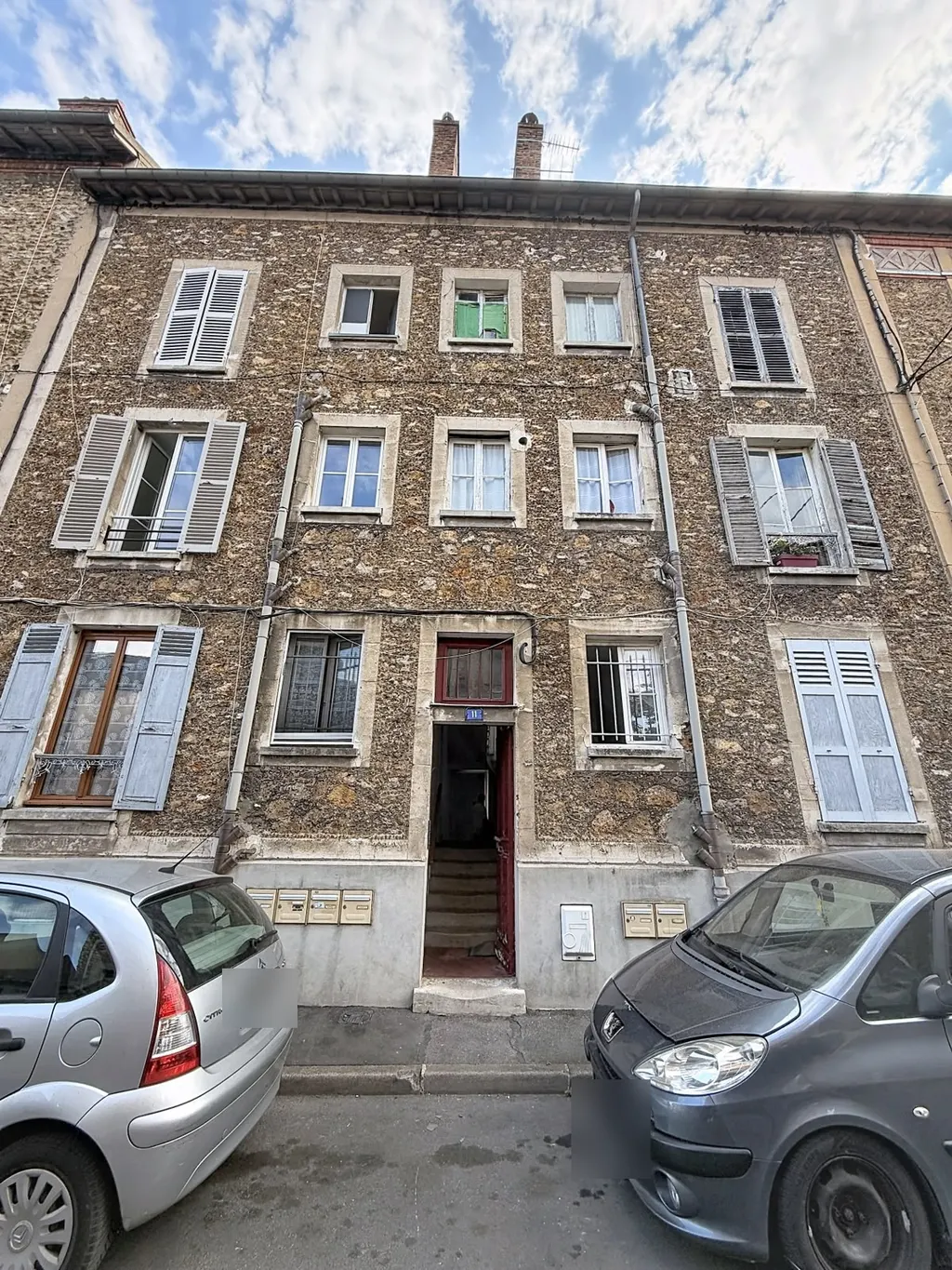 Façade sur rue de l'immeuble en meulière, volets bleu-gris et porte d'entrée rouge