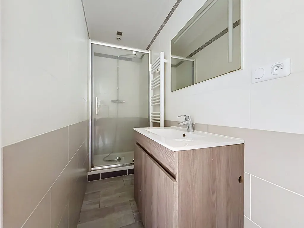 Salle d'eau avec douche vitrée, meuble vasque en bois clair et sèche-serviettes